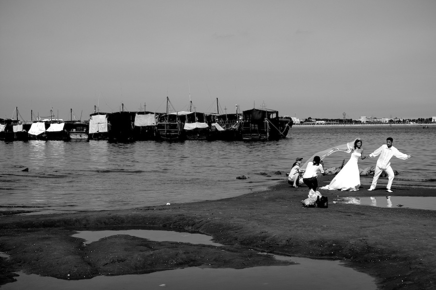 A wedding couple being photographed beside fishing boats