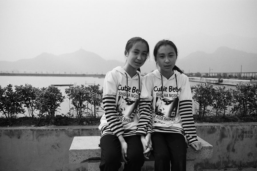 Twin girls seated together beside a lake