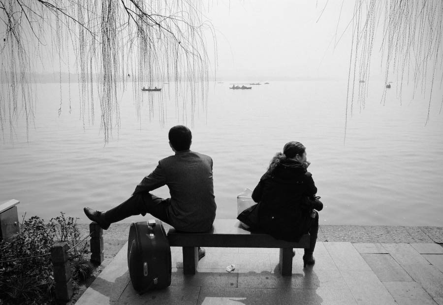 A couple sitting apart on a bench facing West Lake